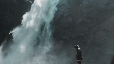 A man standing on a cliff in front of a tall waterfall