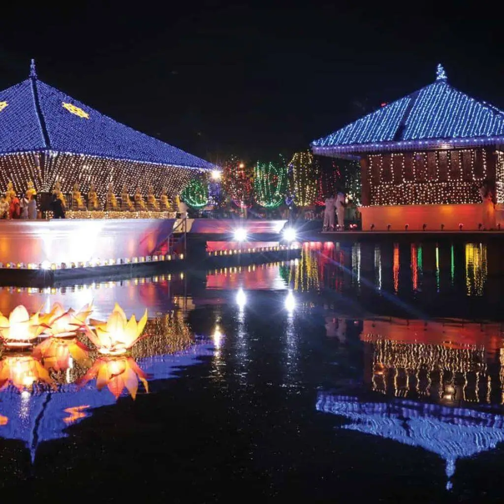 Lit-up lakeside pavilions of the Gangaramaya Temple with floating lotus lanterns at night