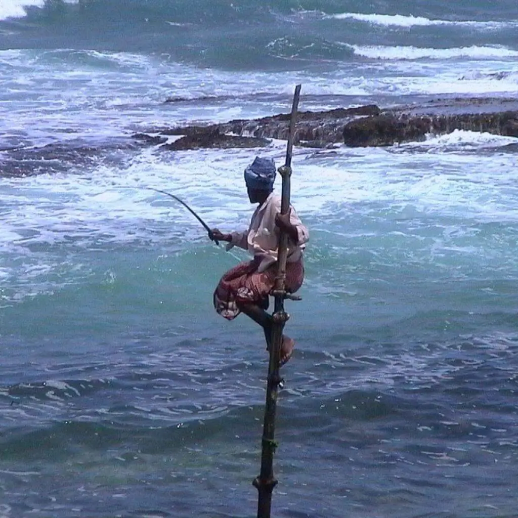 A stilt fisherman perched on a pole above rough surf