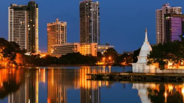 Colombo towers and a white stupa reflected in the lake at dusk