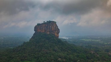 The Sigiriya rock rising above the jungle on a cloudy day, seen from Pidurangala