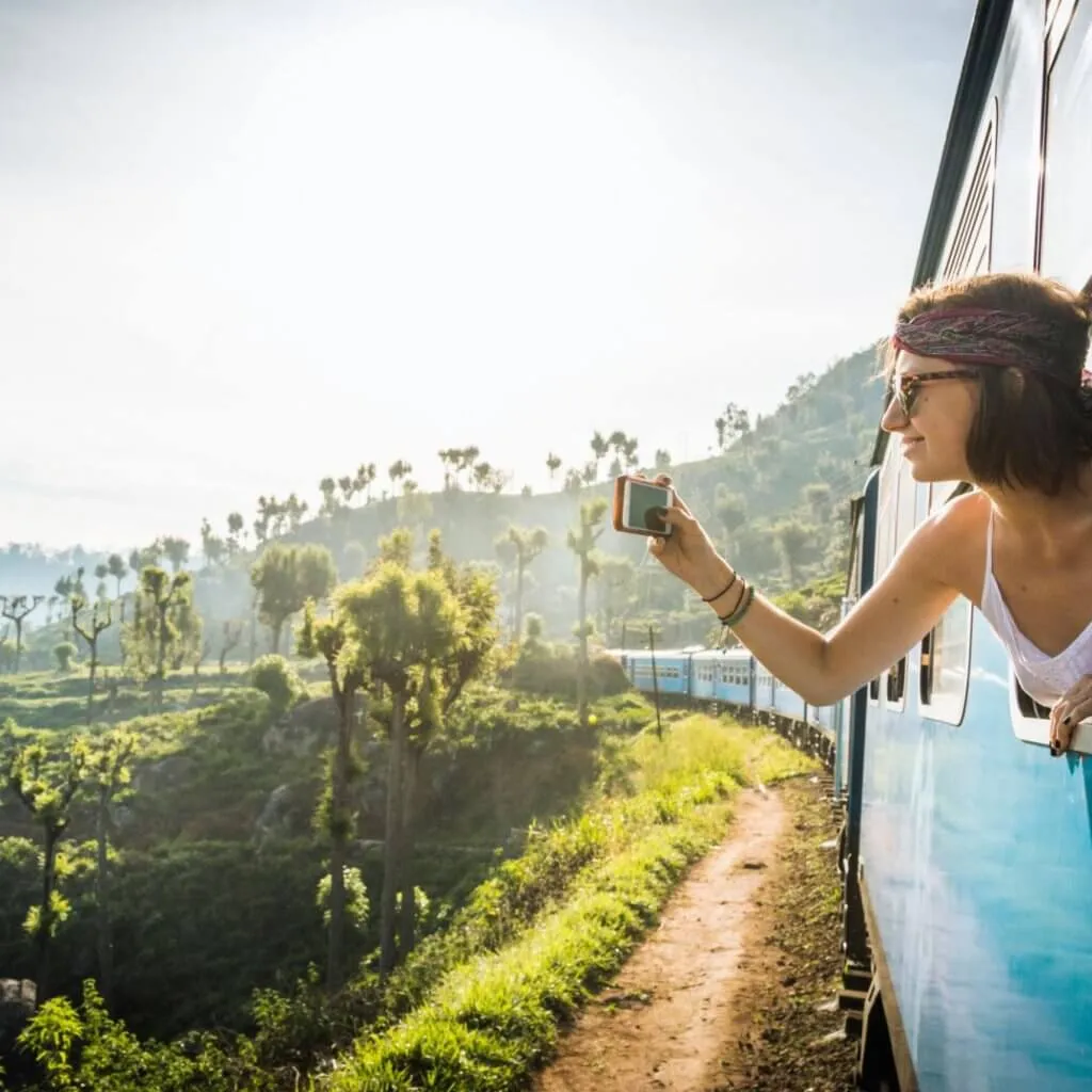 A woman photographing the hills from the window of a blue train
