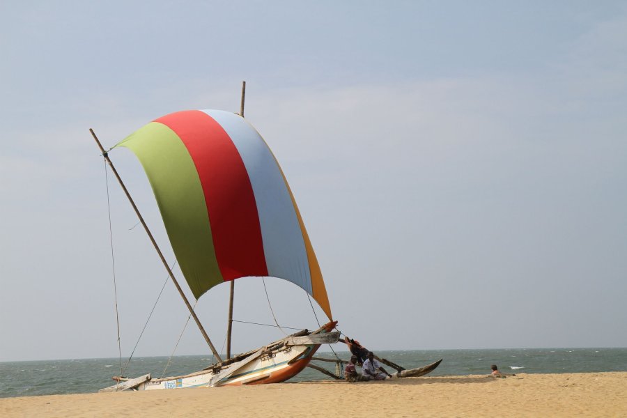 A traditional outrigger boat with a coloured sail on the beach at Negombo